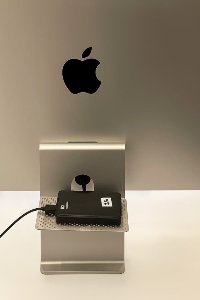Disque dur externe branché à un Mac pour sauvegarde Time Machine, posé derrière un écran Apple Studio Display