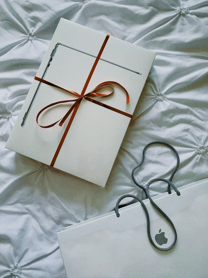 Coffret Apple emballé avec un ruban, posé sur un lit, représentant une idée cadeau pour les fêtes.