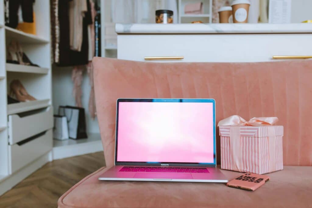 MacBook Pro reconditionné posé sur un canapé rose à côté d'un cadeau de Noël, symbolisant un achat premium pour les fêtes.