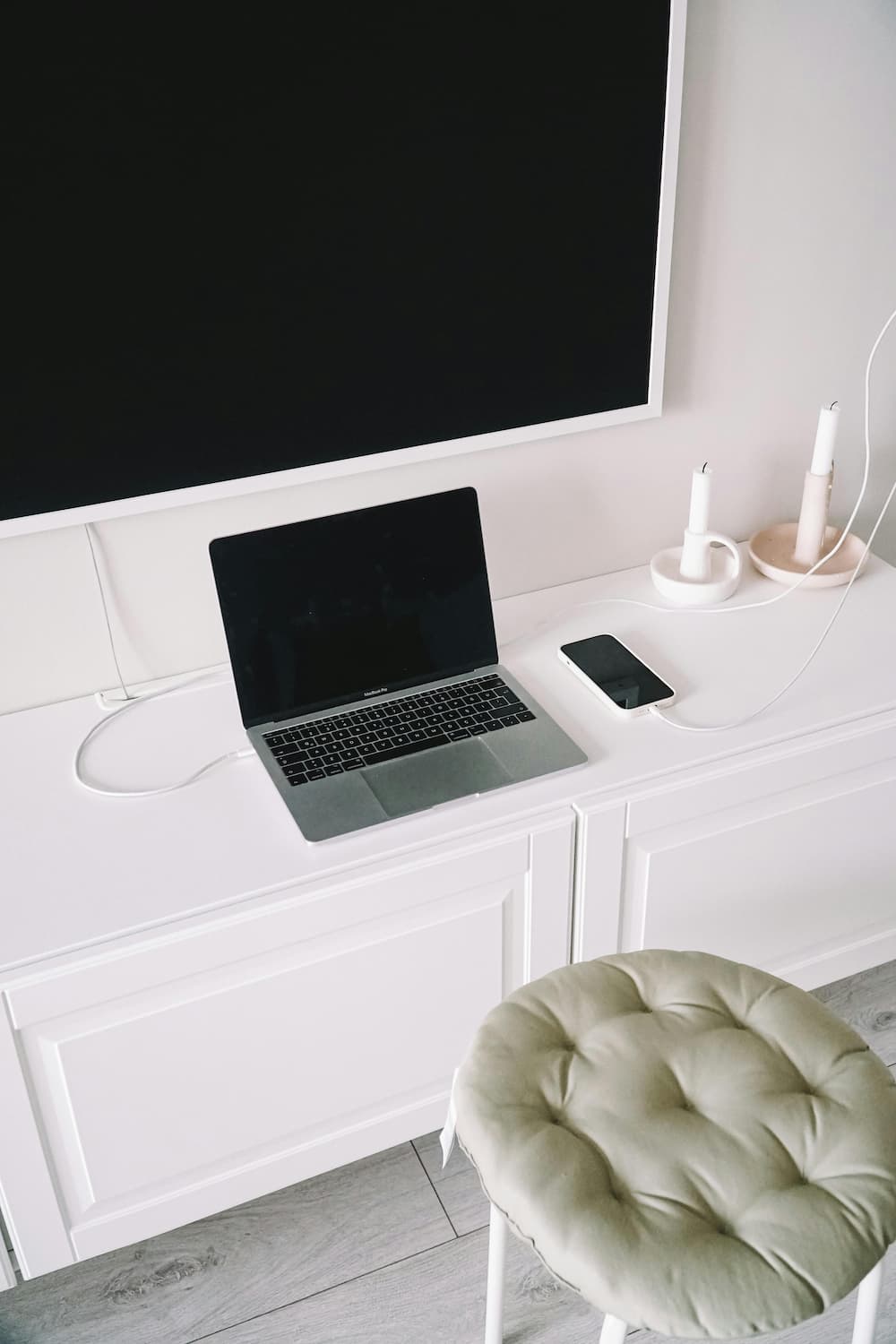 MacBook Pro argenté branché posé sur un bureau blanc avec un iPhone en charge à côté, ambiance minimaliste