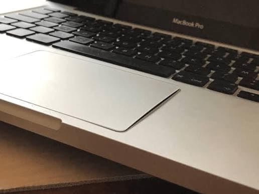 Gros plan sur le trackpad d'un MacBook Pro légèrement soulevé et déformé, indiquant une batterie gonflée à remplacer d'urgence