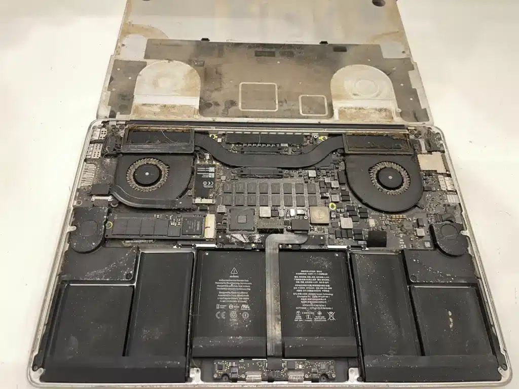 Intérieur d'un MacBook Pro A1398 de 2015 ouvert, avec de la poussière accumulée sur les deux ventilateurs et les composants
